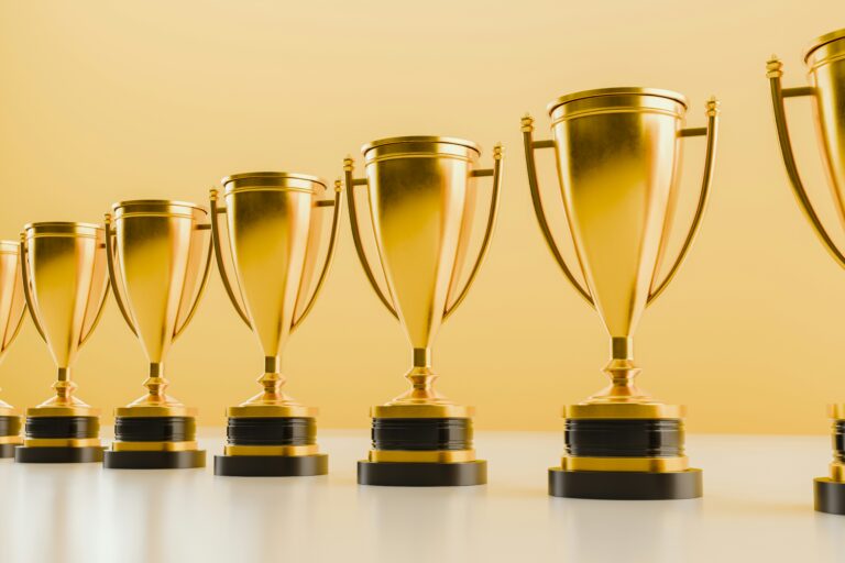 A row of golden trophies lined up against a smooth yellow background, symbolizing achievement and success. This image represents excellence and recognition, similar to the IDC FinTech Rankings: Top 100, which highlights the top-performing companies in the financial technology sector.